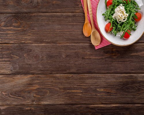 A wooden table with a plate of fresh salad, beans and corn tortillas